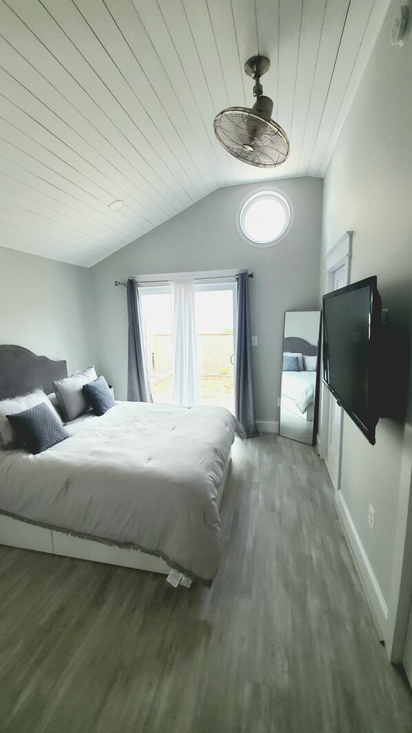 A bedroom with a bed, a ceiling fan, a TV, and a window with curtains. - Luxury Cottage w/ Bay & Boardwalk Views--steps from the water (North Beach)