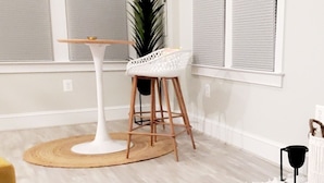 A room with a white ceiling, large windows with blinds, a white chair, a small table, and a potted plant. - Luxury Cottage w/ Bay & Boardwalk Views--steps from the water (North Beach)