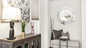 A living room with a dark wood console table, a floor lamp, a potted plant, a round mirror, a gray sofa, and a small side table. - Milton Home away from home (Milton)