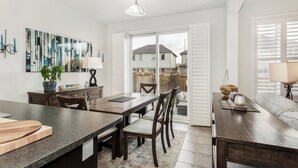 A modern kitchen with a dining area, featuring a large window, a dining table with chairs, a kitchen island, and a view of the backyard. - Milton Home away from home (Milton)