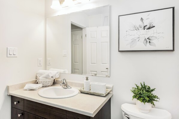 A bathroom with a white sink, dark wooden vanity, a white toilet, a framed floral artwork, and a potted plant.