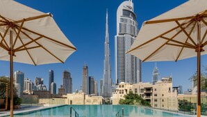 A poolside area with lounge chairs and umbrellas, overlooking a cityscape with modern skyscrapers. - The Dubai EDITION (Dubai)