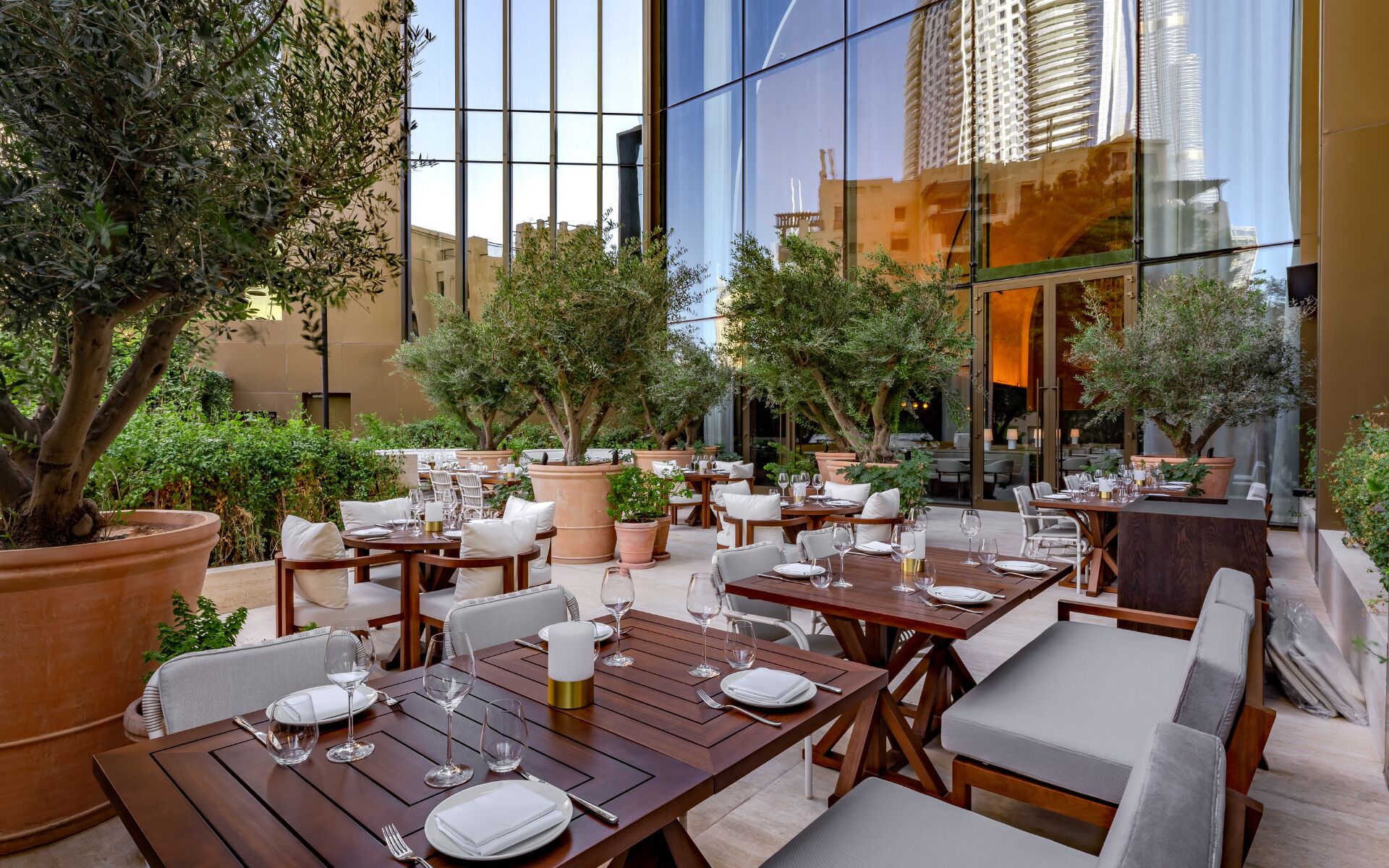An outdoor dining area with tables and chairs, surrounded by potted plants and trees.