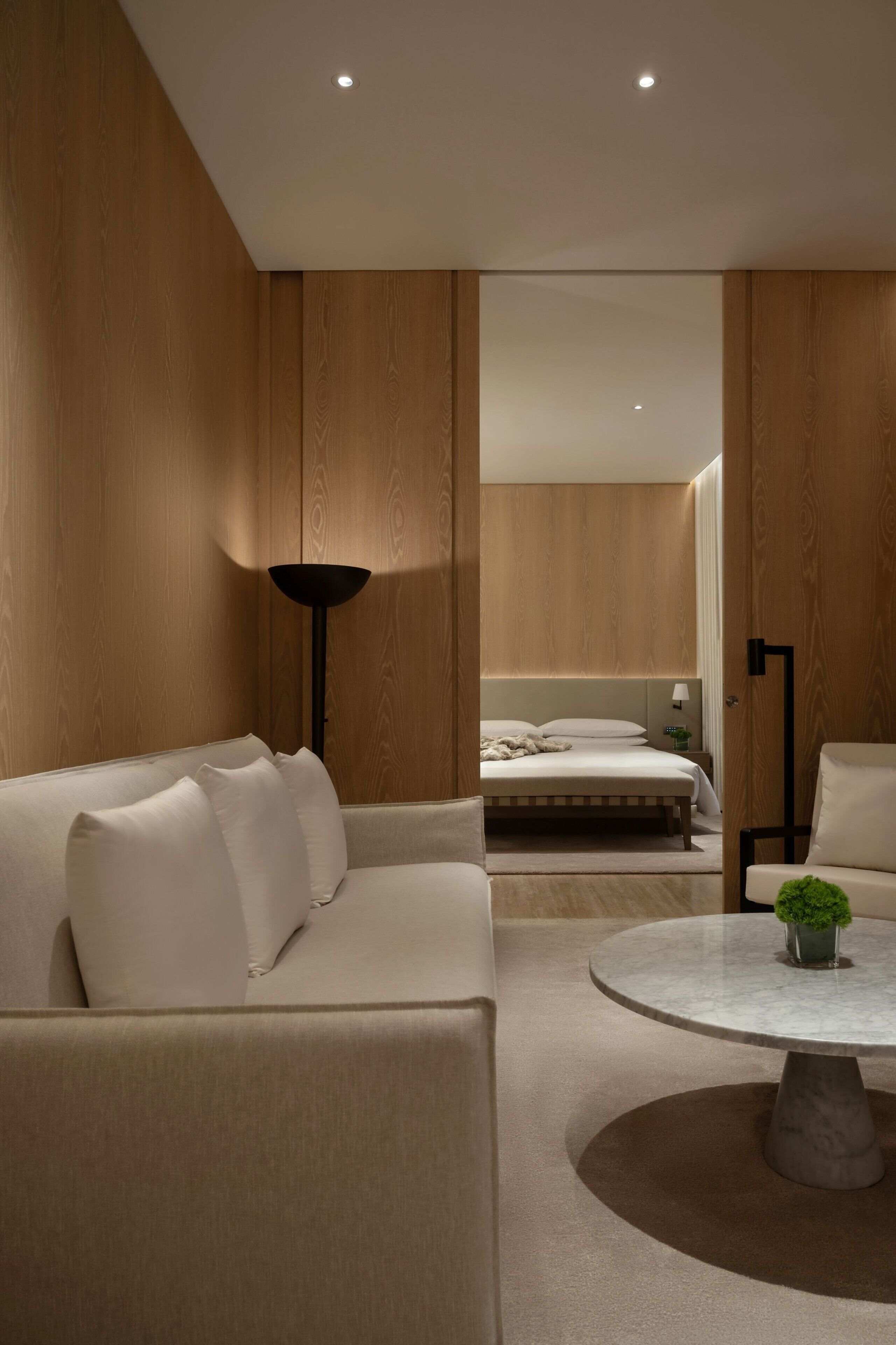 A modern hotel room with a large bed, a sofa, a round coffee table, and a lamp.