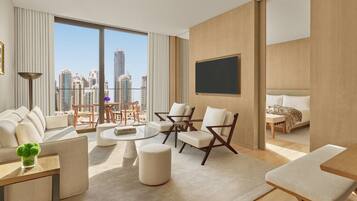A modern hotel room with a large window offering a city view, a sofa, a dining table, and a bed.