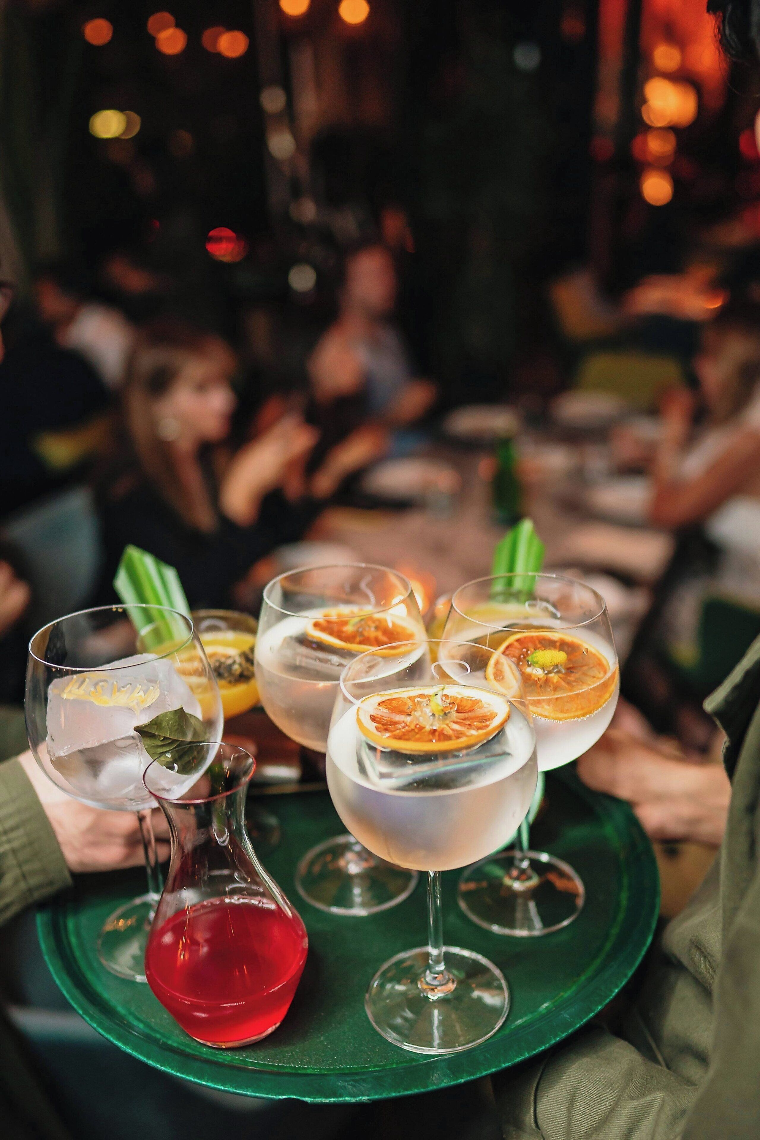 A tray with several glasses of cocktails, garnished with citrus slices and herbs, on a green tray.