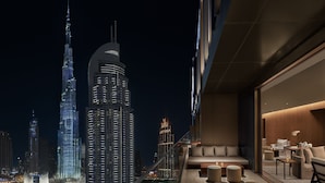 A high-rise building with a modern interior featuring a balcony with seating and tables, overlooking a cityscape at night. - The Dubai EDITION (Dubai)