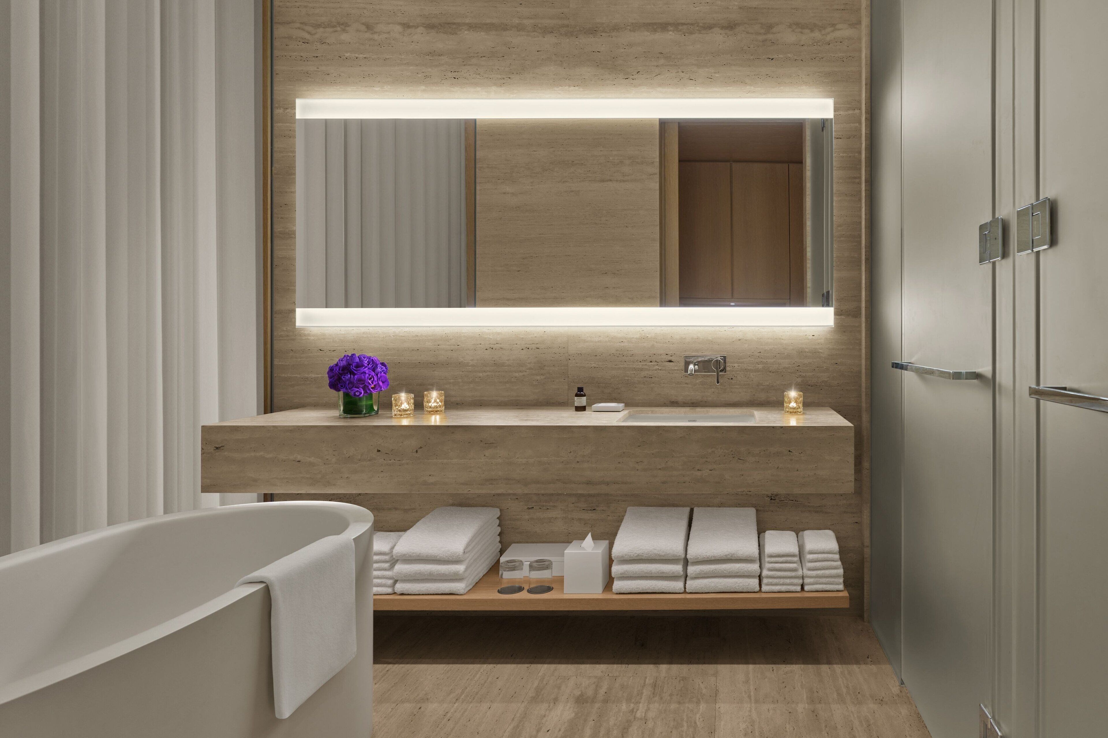 Un baño moderno con tocador de madera, un espejo grande, una bañera y toallas dobladas cuidadosamente.