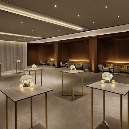 A modern hotel lobby with multiple seating areas, tables with floral centerpieces, and a warm ambient lighting.