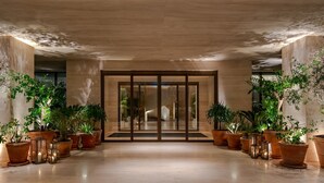 A spacious lobby with a modern design, featuring a large glass door, multiple potted plants, and a polished floor. - The Dubai EDITION (Dubai)