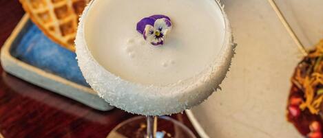 A dessert with a white, frosted top and a purple garnish, accompanied by waffles and a bowl of soup.