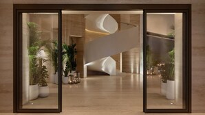 A modern lobby with a central spiral staircase, potted plants, and a polished wooden floor. - The Dubai EDITION (Dubai)