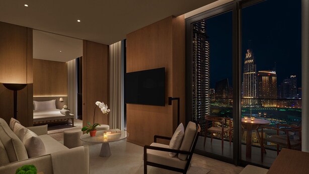 A modern hotel room with a large window offering a city view, a comfortable sofa, a small table with a plant, and a flat-screen TV mounted on the wall. - The Dubai EDITION (Dubai)