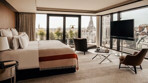 A modern hotel room with a large bed, a TV, a chair, and a view of a cityscape. - Bvlgari Hotel Paris (Paris)