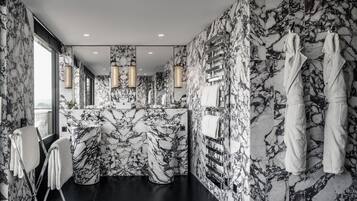 Un baño moderno con paredes de mármol y piso negro, que incluye un lavamanos, espejo, toallero y un amplio ventanal.