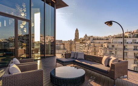 A modern rooftop terrace with a large glass wall, a sectional sofa, a round coffee table, and a street lamp.