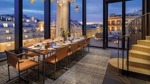 A rooftop dining area with a long table set for six, overlooking a cityscape at dusk. - Bvlgari Hotel Paris (Paris)