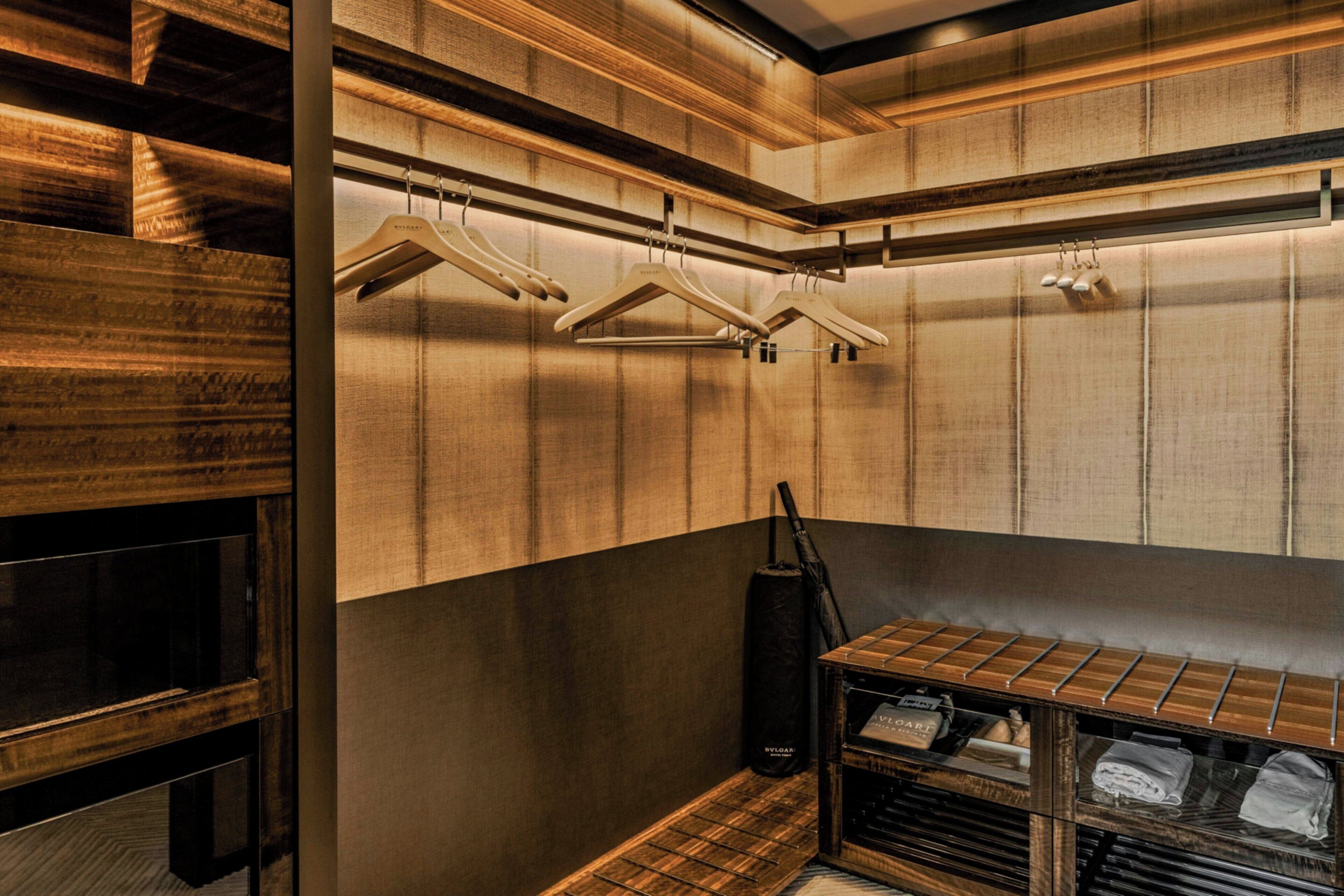 A room with wooden panel walls, a hanging rack with clothes, a black bag, and a shelf with folded clothes.