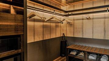 A room with wooden panel walls, a hanging rack with clothes, a black bag, and a shelf with folded clothes.