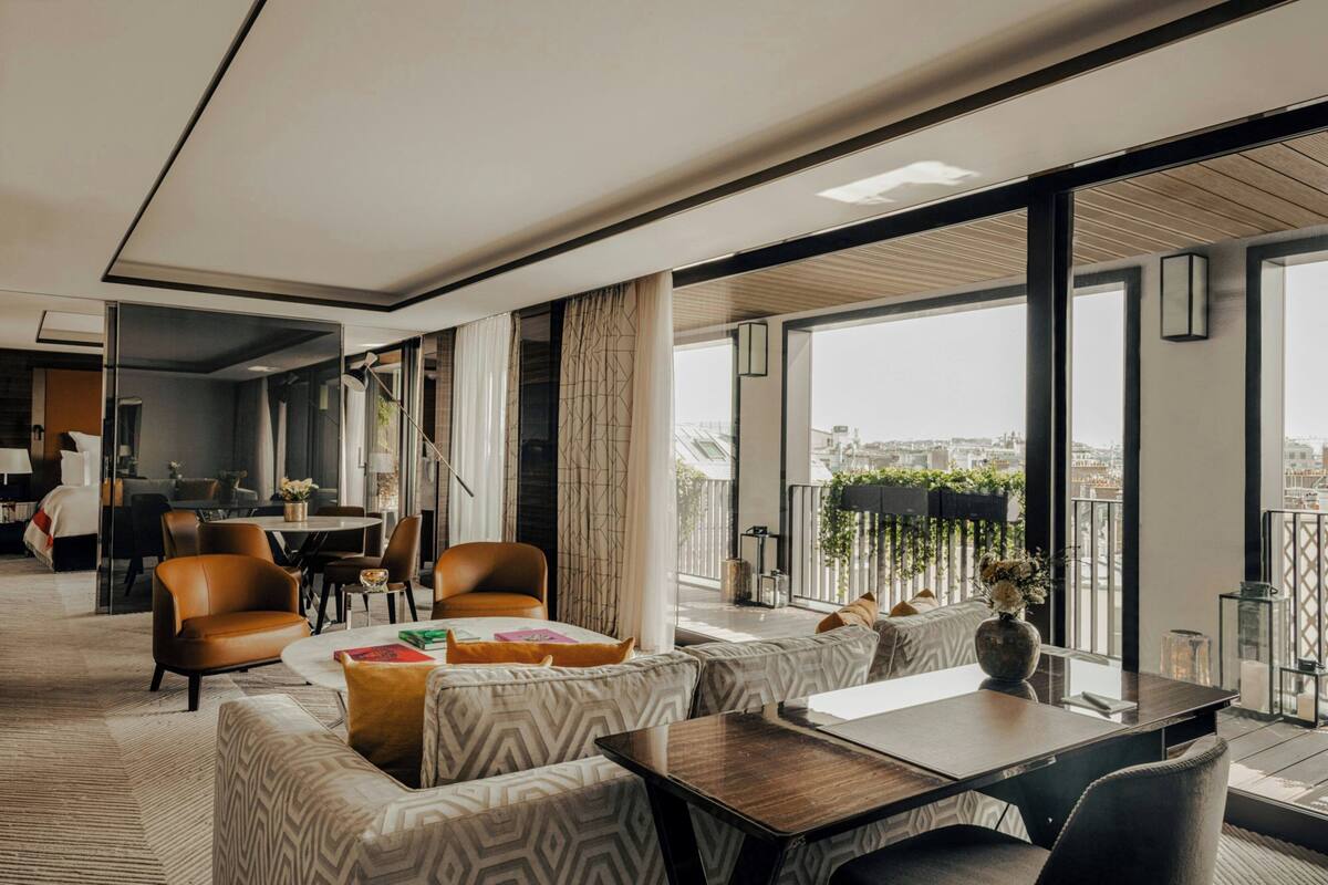 A modern hotel room with a large balcony, a dining area, and a view of the city.