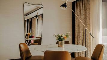 A dining area with a round table, two chairs, a mirror, a vase with flowers, and a lamp.