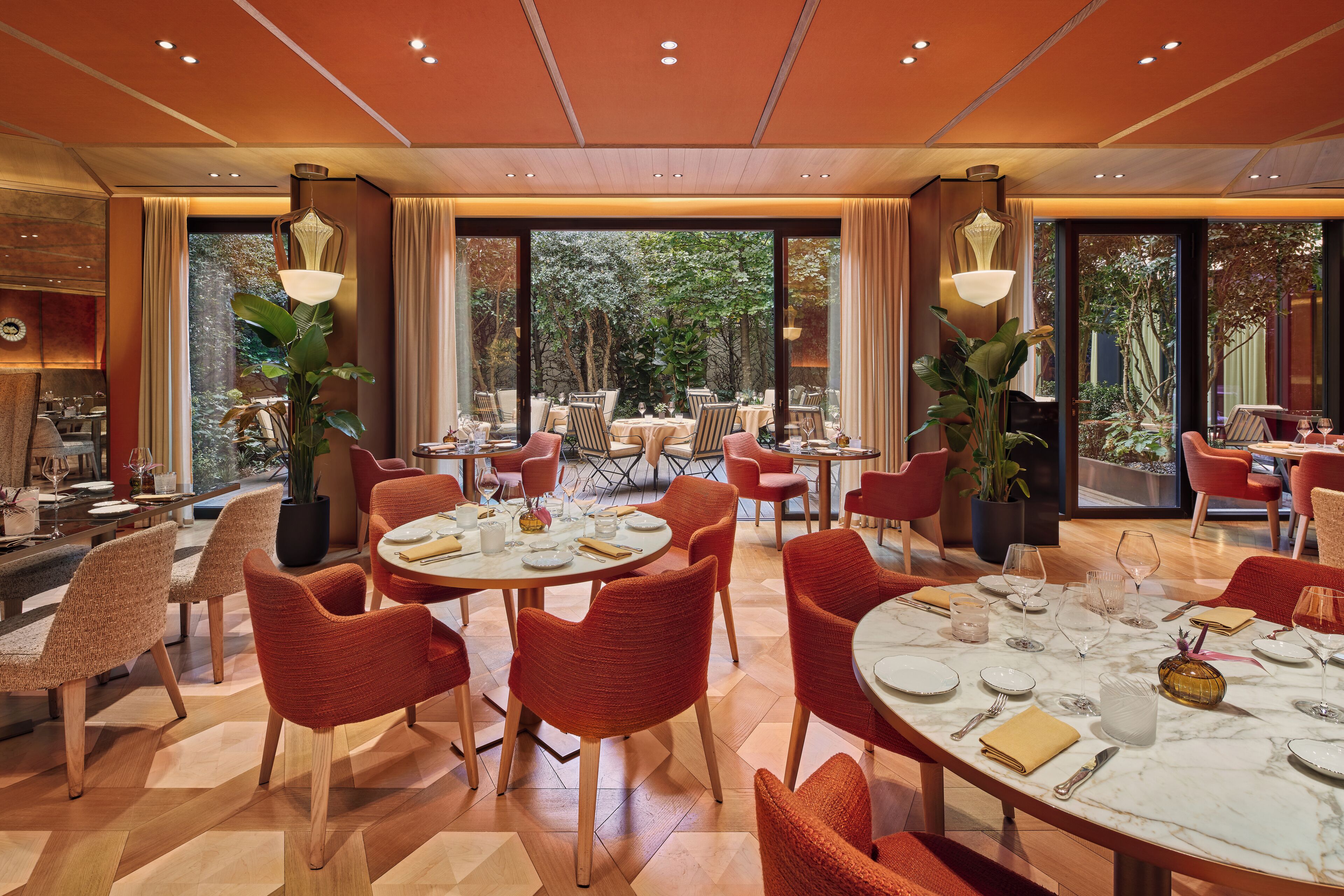 A dining area with round tables, red chairs, and large windows offering a view of the outdoors.