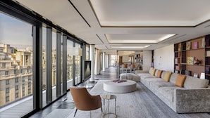 A modern living room with a large window, a sofa, a coffee table, and a bookshelf. - Bvlgari Hotel Paris (Paris)