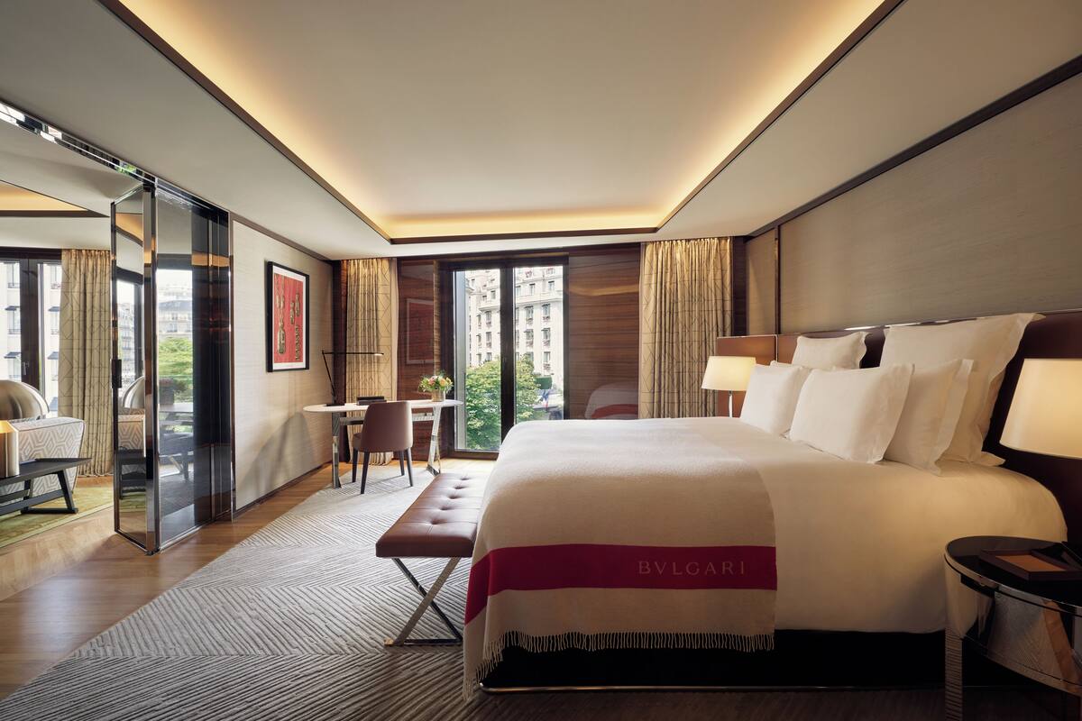 A modern hotel room with a large bed, a desk, and a seating area.