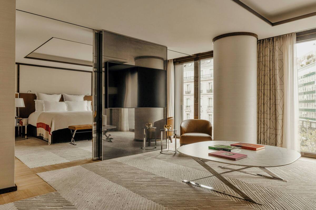 A modern hotel room with a bed, a dining table, and a view of the city.