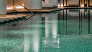 Een modern binnenzwembad met helder water, grote cilindervormige kolommen en minimalistische zitplaatsen.