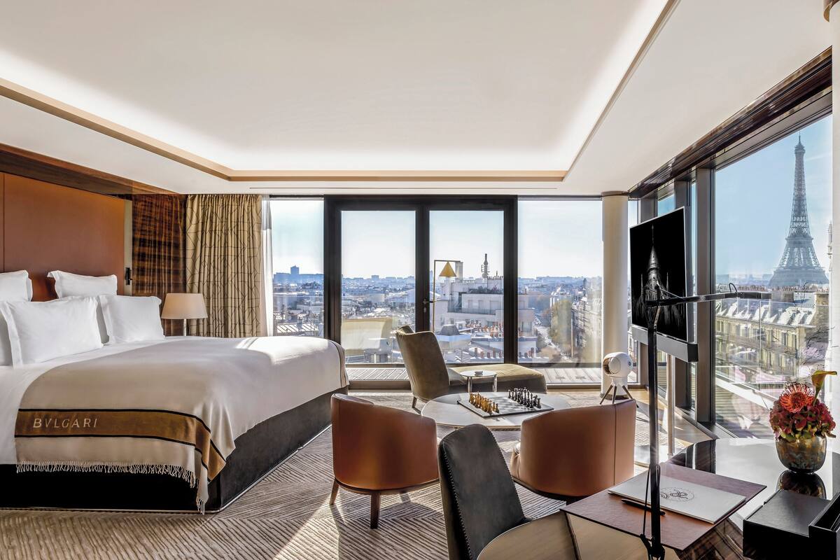 A hotel room with a large bed, a desk, a chair, a TV, and a view of the Eiffel Tower.