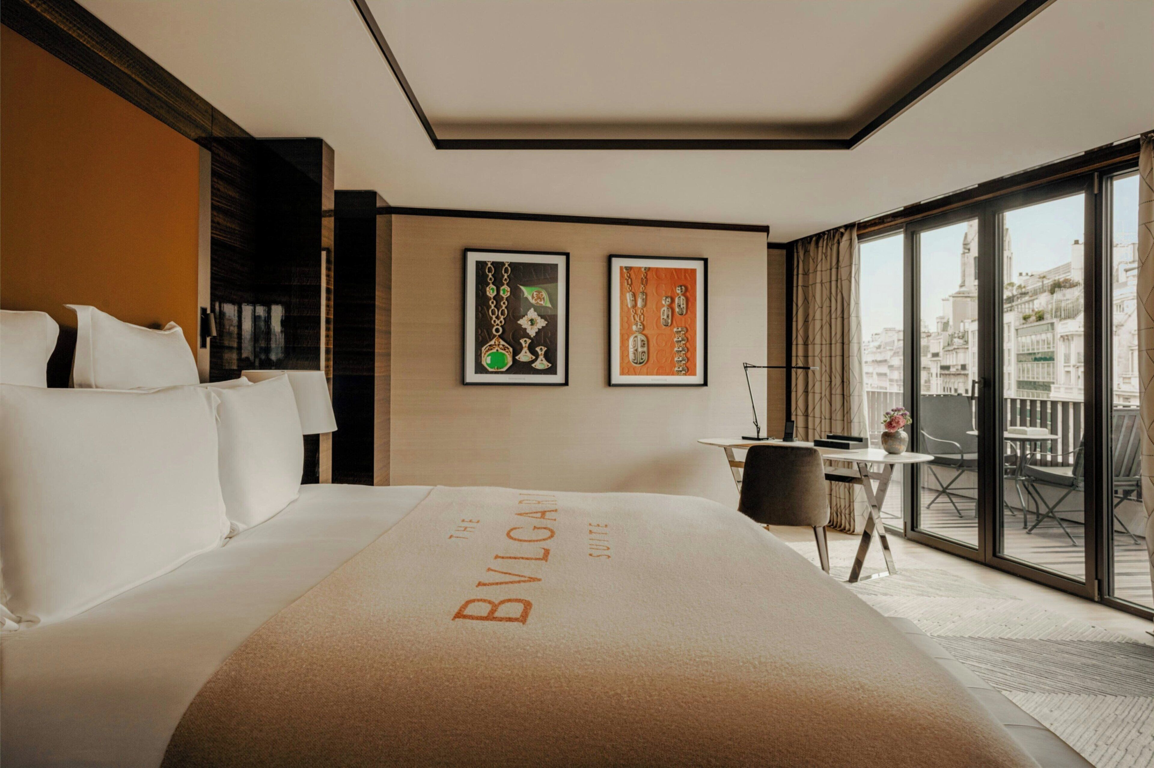 Habitación de hotel con una cama grande, un escritorio y vistas de la ciudad a través de amplias ventanas.