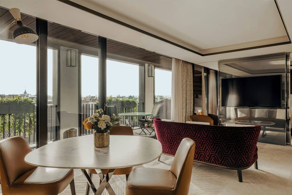 A modern living room with a round table, leather chairs, a red patterned sofa, and a TV.