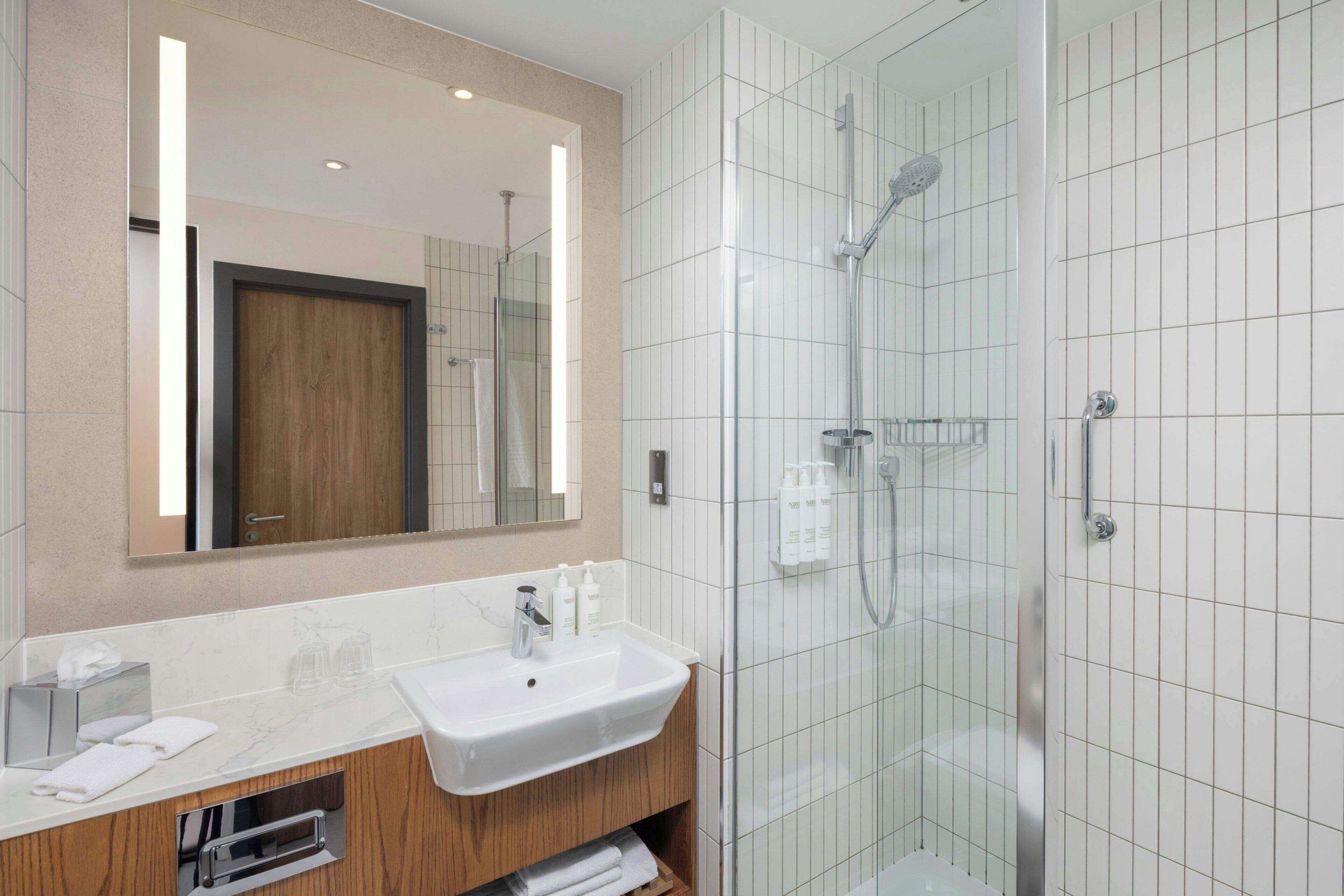 A modern bathroom with a white sink, mirror, and glass shower enclosure.