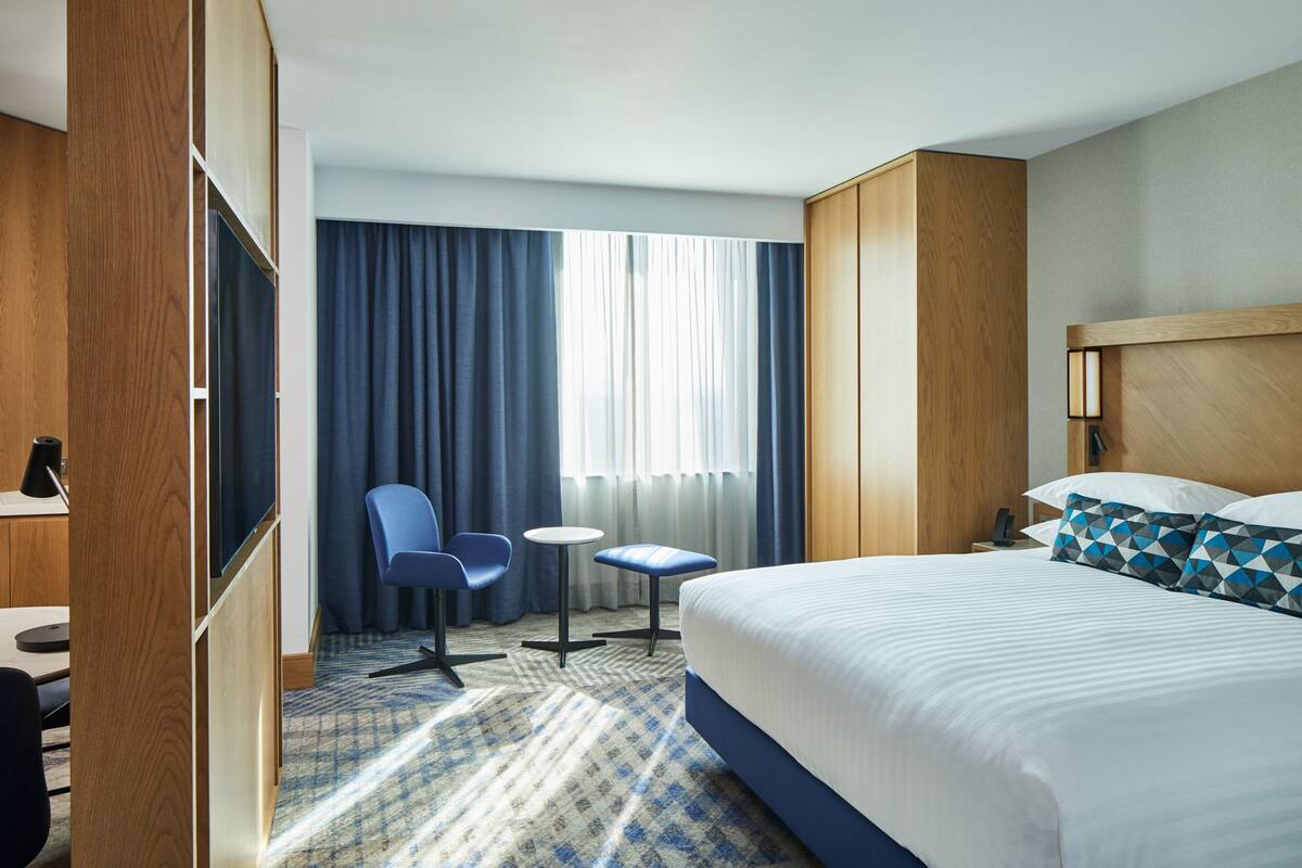 Una habitació d'hotel amb un llit gran, un escriptori amb una cadira, una taula petita i una televisió.