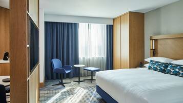 Una habitación de hotel con una cama grande, un escritorio con una silla, una mesita y un televisor.