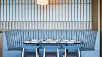 A restaurant with a blue upholstered booth seating area, a round table set with glasses and plates, and a wooden slat wall with hanging lights.