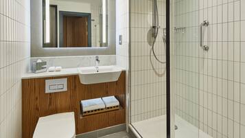 A modern bathroom with a white sink, wooden vanity, a toilet, and a glass-enclosed shower area.