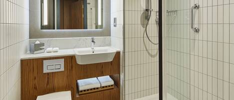 A modern bathroom with a white sink, wooden vanity, a toilet, and a glass-enclosed shower area.