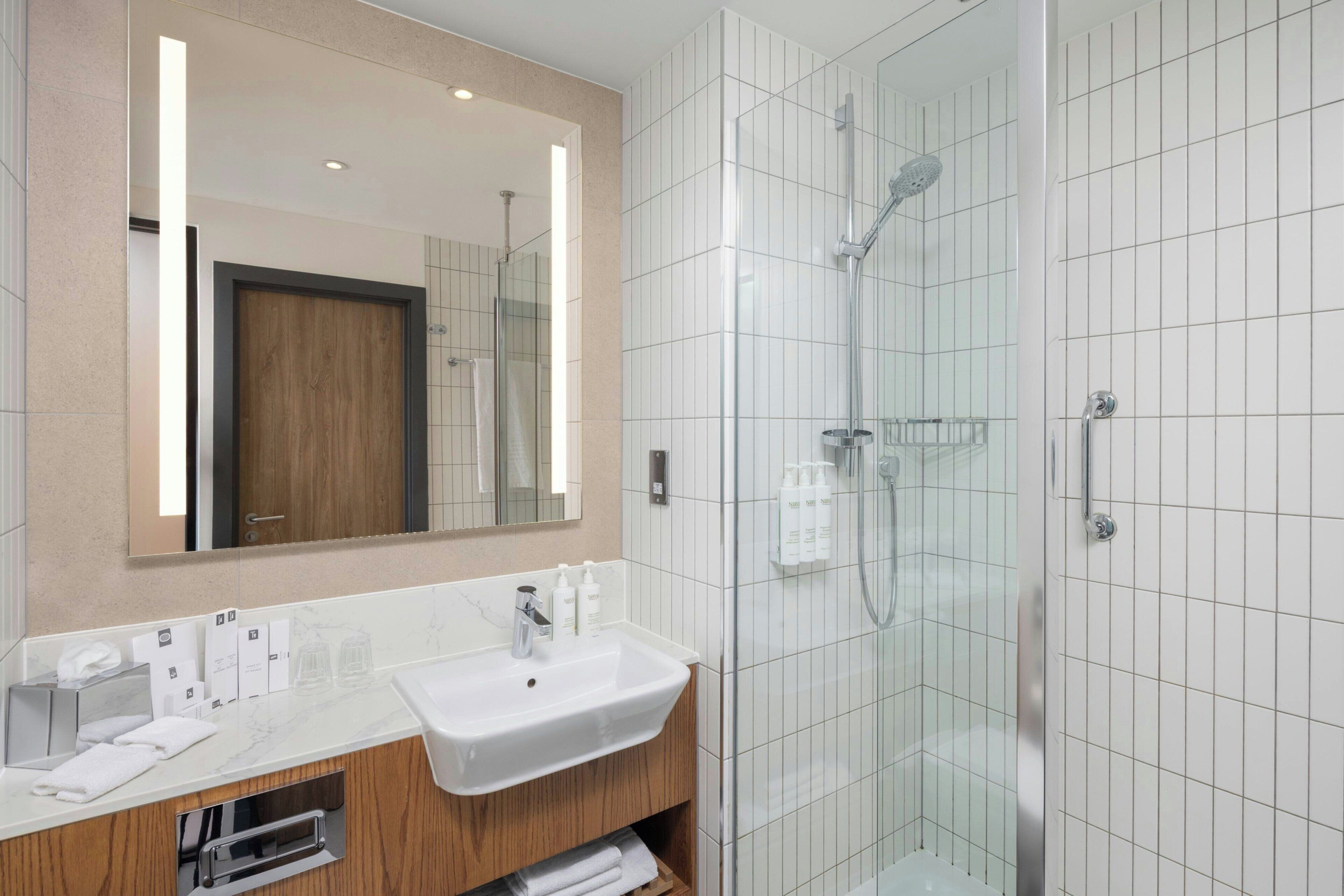 A modern bathroom with a glass-enclosed shower, a white sink, and a wooden vanity.