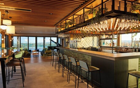 A modern bar area with high stools, a piano, and a view of the city.