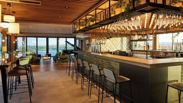 Un área de bar moderna con taburetes altos, un piano y vistas a la ciudad.