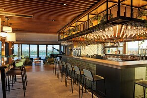 A modern bar area with high stools, a piano, and a view of the city. - Courtyard by Marriott Exeter Sandy Park (Exeter)