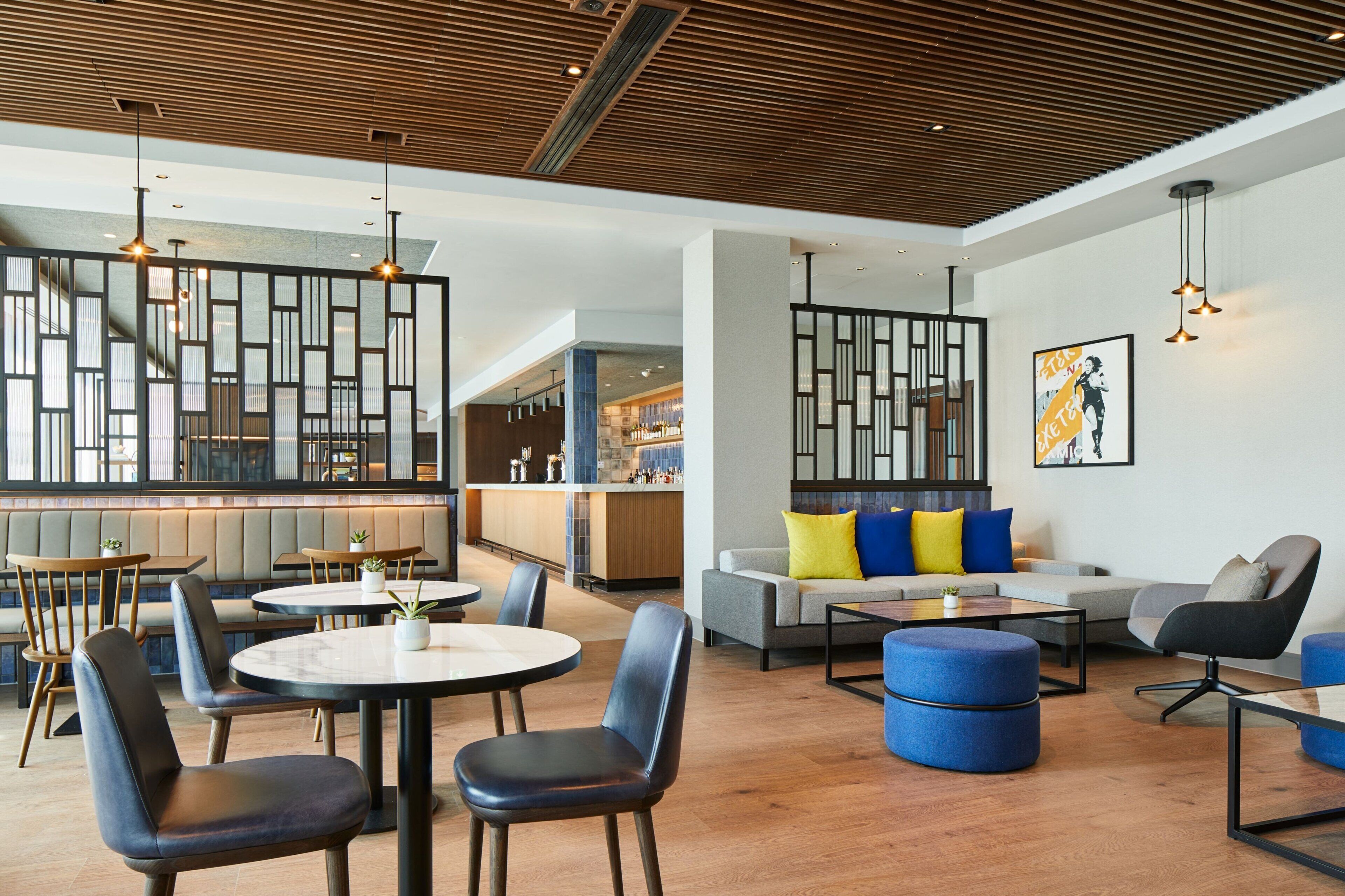 A modern hotel lobby with round tables, comfortable seating, and a bar area.