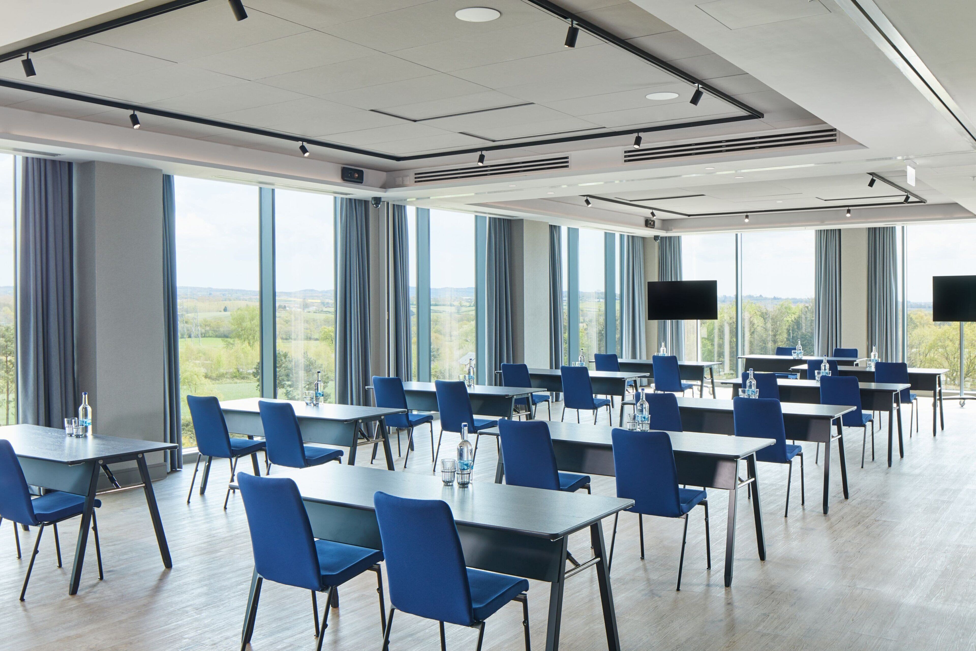 A conference room with tables and chairs, large windows, and a view of the outdoors.
