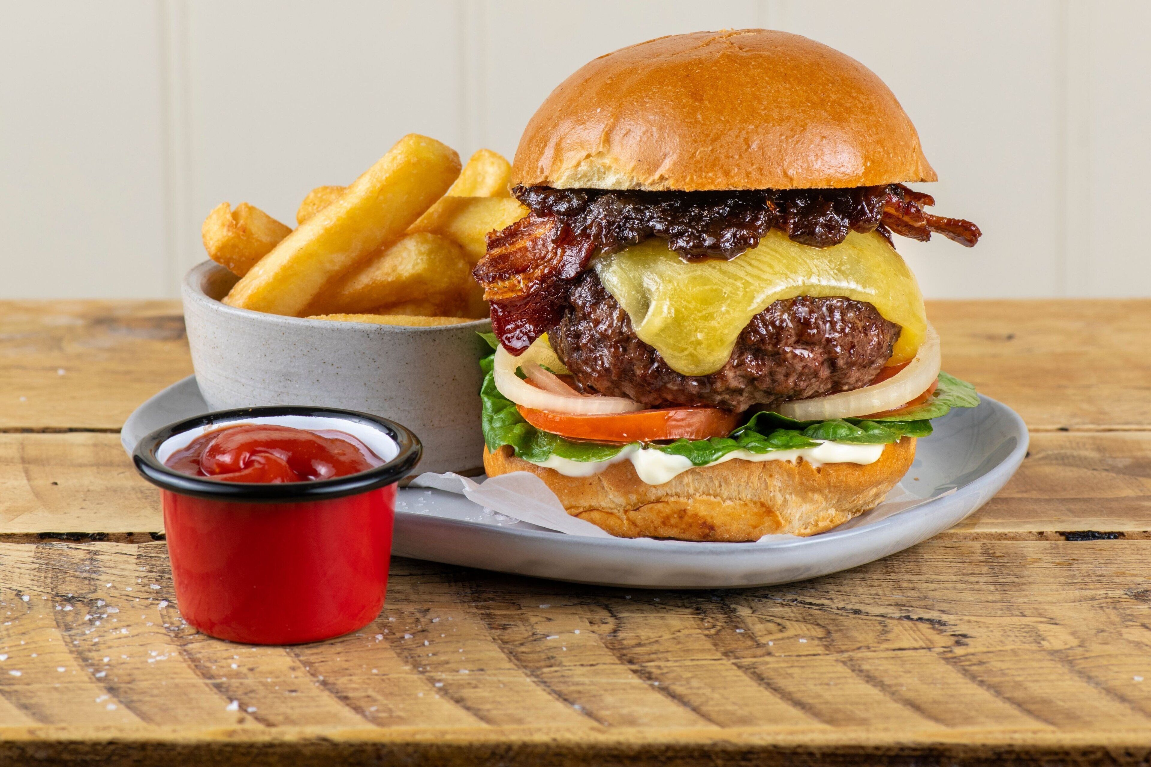 A burger with fries and ketchup on a wooden table.