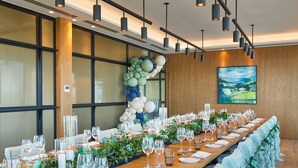 Una larga mesa de banquete dispuesta para un evento formal, con un arco decorativo de globos y un cuadro grande en la pared.
