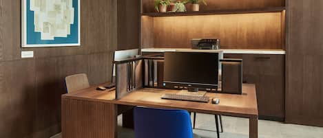 Un espace de bureau moderne avec un bureau en bois, une chaise bleue, un ordinateur et un tableau d’affichage où sont accrochés des documents.