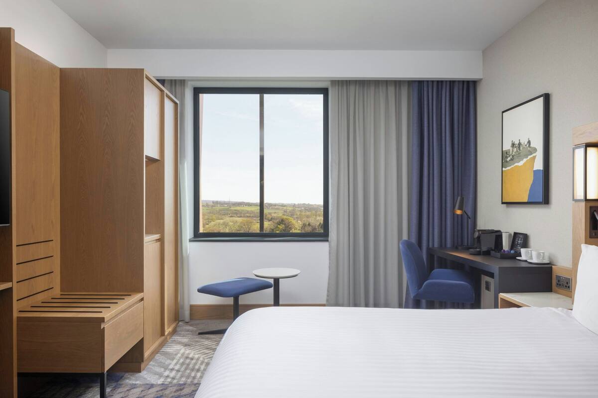 Habitació d'hotel amb llit, escriptori, cadira, taula petita i armari.