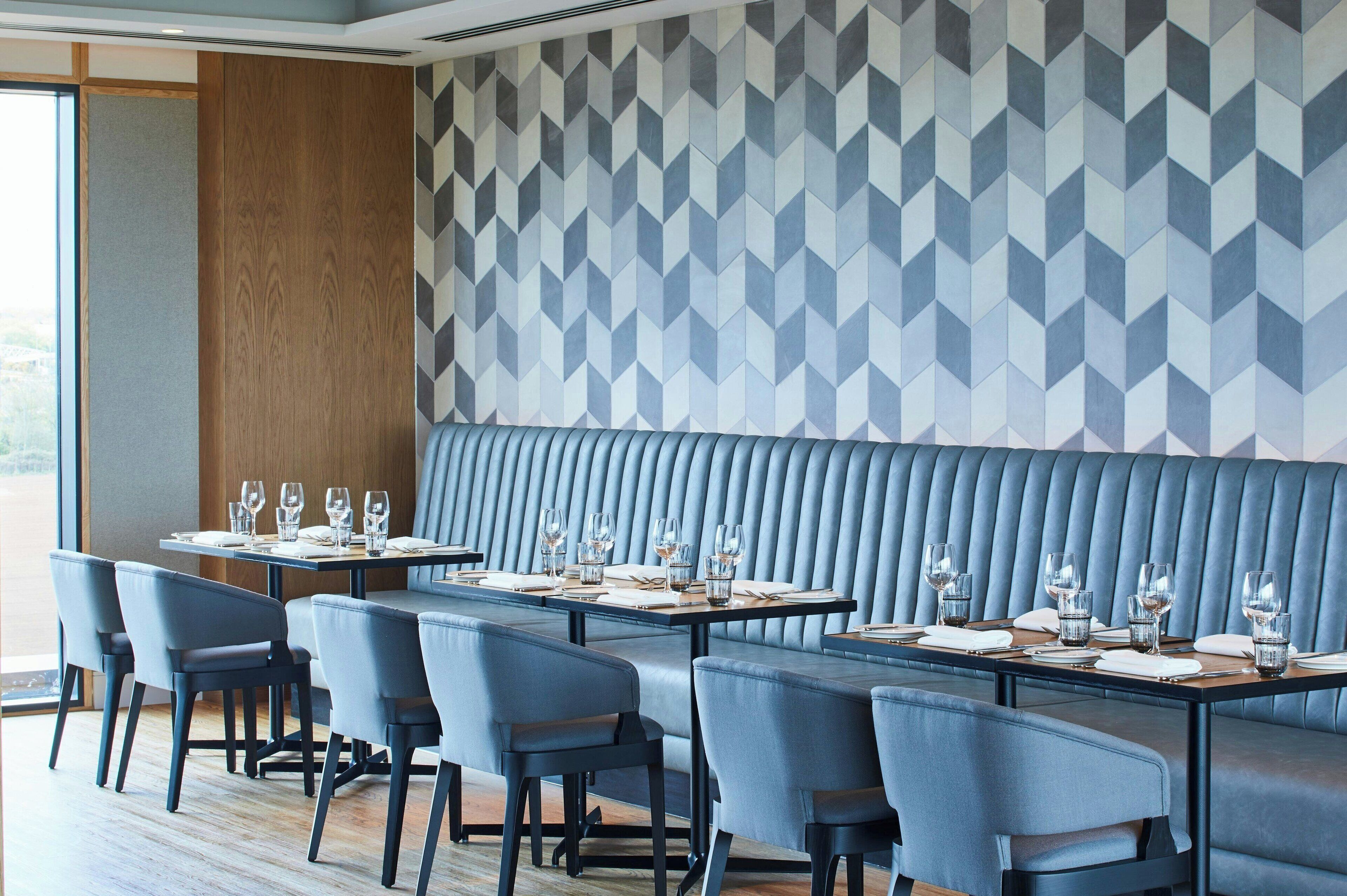 Restaurante moderno com um balcão comprido, cabines estofadas em azul e parede com padrão geométrico.